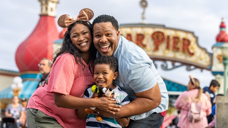 A family laughs in glee while standing in front of Pixar Pier at Disney California Adventure Park