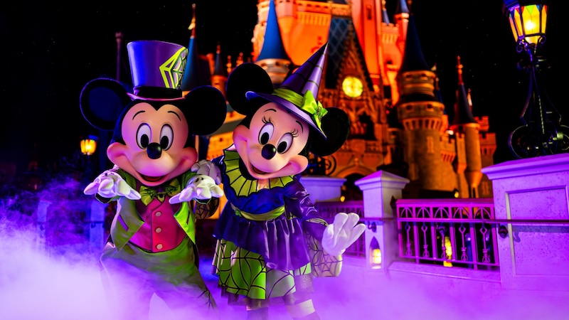 Minnie Mouse and Mickey Mouse wearing Halloween outfits and posing in front of Cinderella Castle