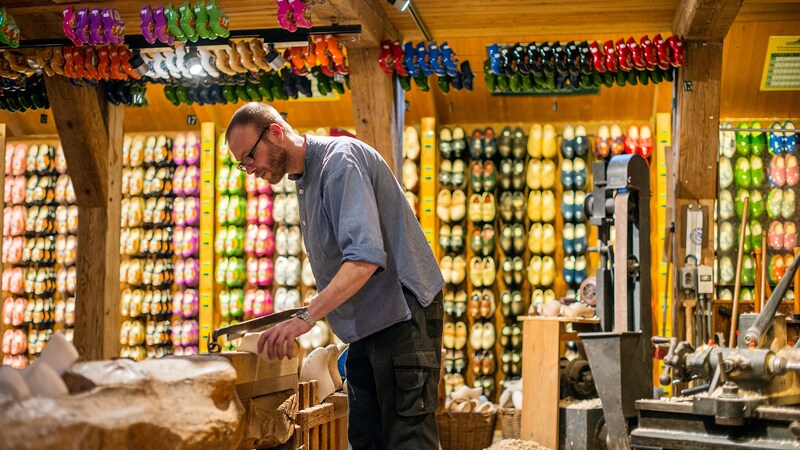 A shoemaker uses his tools in a shoe shop with its ceiling and a wall filled with wooden shoes
