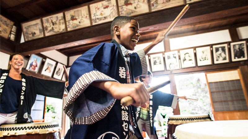 A young boy in a traditional robe holds drumsticks as he plays a taiko drum in Japan