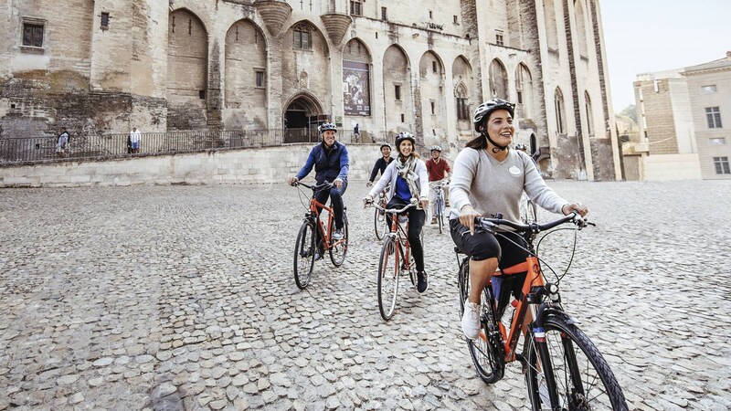 Five people ride bikes on a cobblestone street