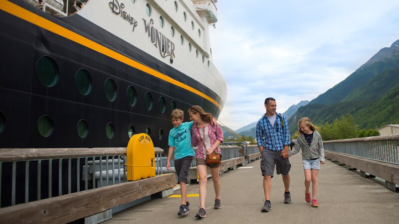 A young family of 4 walking alongside a docked Disney cruise ship in a mountainous setting
