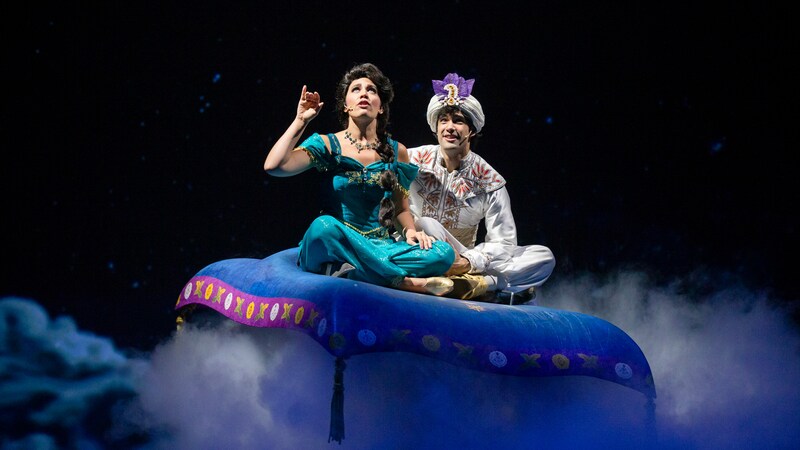 A scene from a live stage show featuring Jasmine and Aladdin on a flying carpet