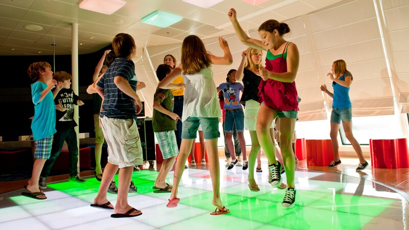 Tween kids talk on comfortable lounge chairs with flat screen monitors in the background