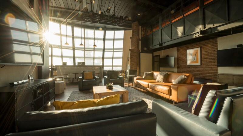 A cozy recreation room with a jumbo screen TV, large windows and overstuffed chairs and couches