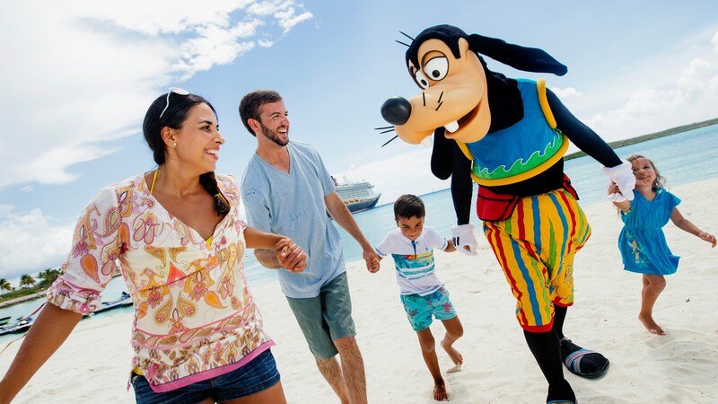 Goofy dressed in tropical attire while walking on a beach with a smiling young family of 4