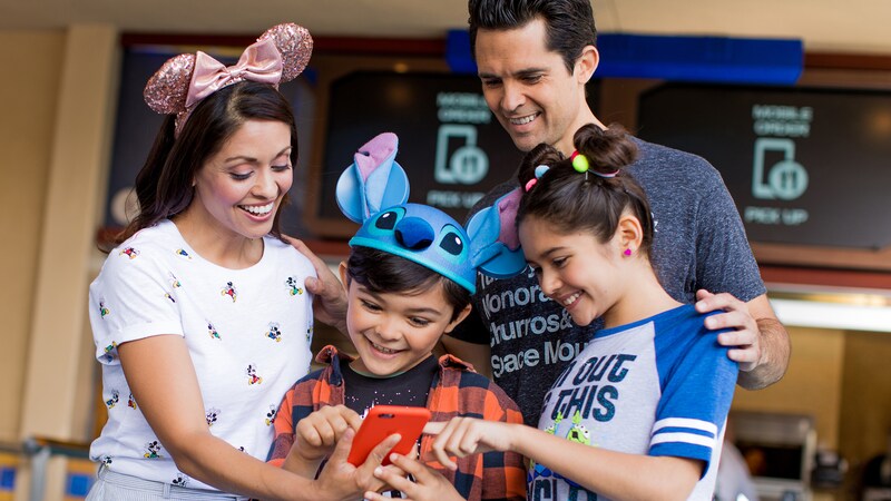 A family stands in front of a restaurant counter and looks at a mobile phone, and both children touch the screen