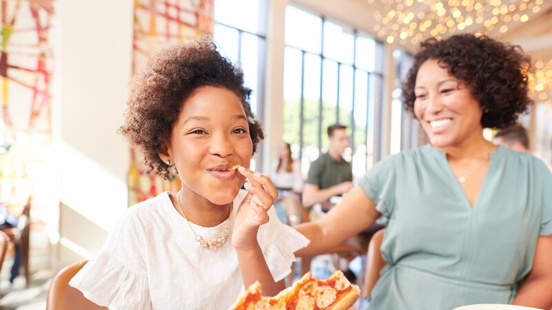 A mom and her daughter sitting at a table enjoying pizza and spaghetti