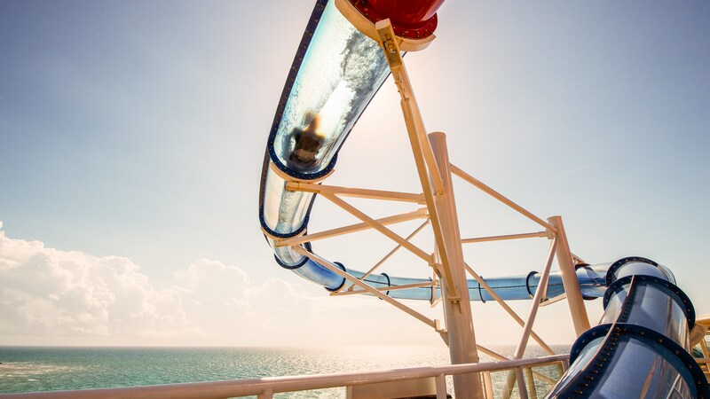 A Guest watersliding through a translucent tube extended over the side of the ship overlooking the ocean