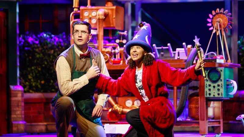 A daughter wears a sorcerers hat and holds a magic wand as she sings to her father