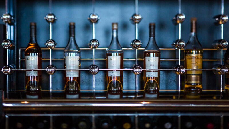 A man and a woman hold hands and share a laugh while seated at the bar of a cozy lounge