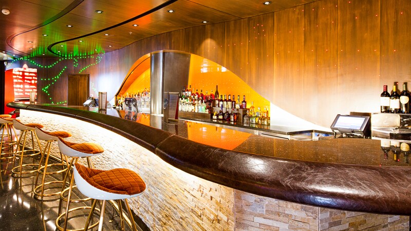 A long, curved bar has several stools and a lit back wall