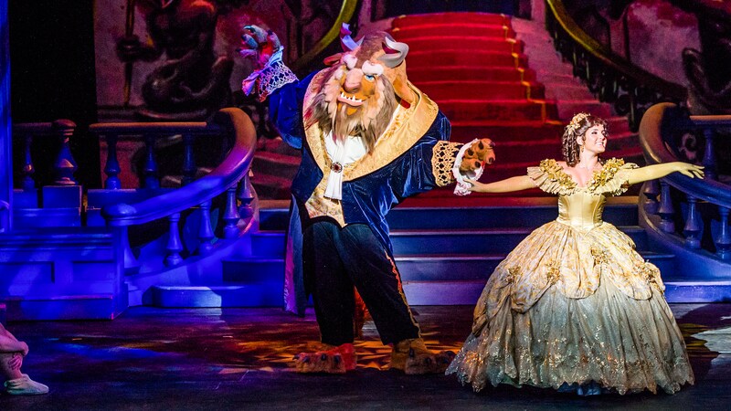 The Beast dances with Belle in front of a grand staircase