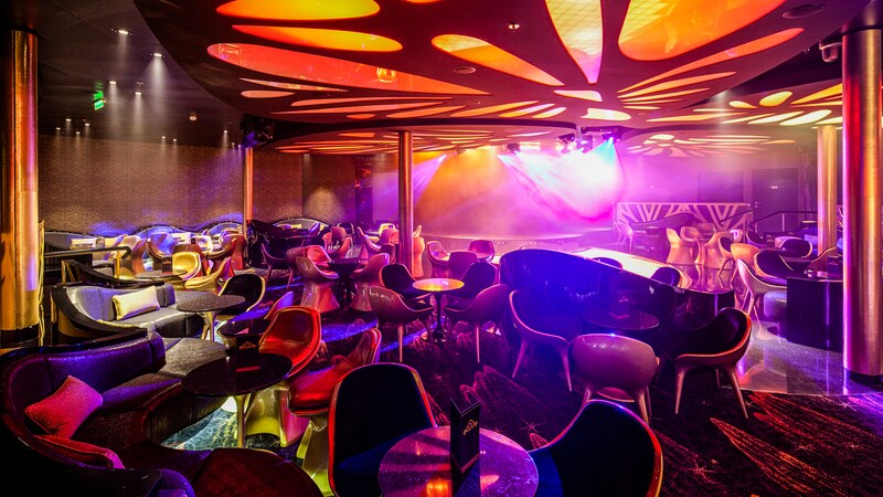 A nightclub features lots of seating, a dance floor and high energy lighting
