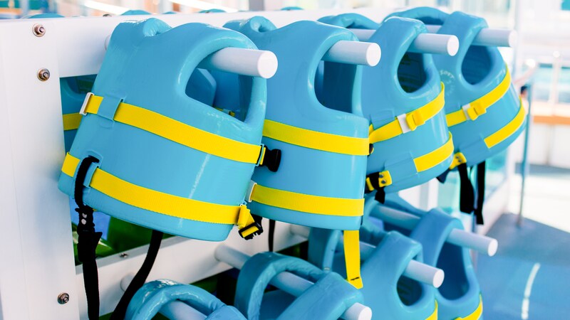 Eight toddler sized pool vests hanging on horizontal poles
