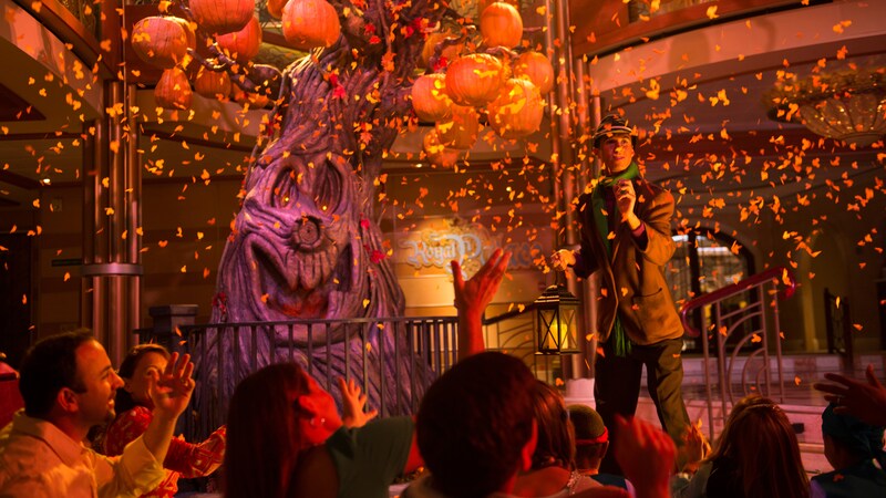 Families watch a Halloween themed show with a spooky tree, jack o lanterns, orange light and confetti