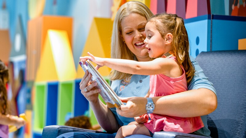 A Cast Member reads a book to a little girl, at Its a Small World Nursery on the Disney Dream