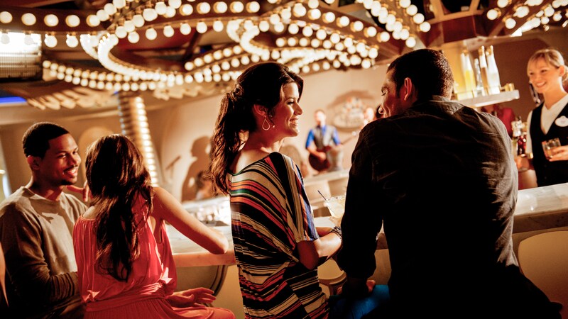 Two couples talk while waiting for drinks at a brightly lit bar