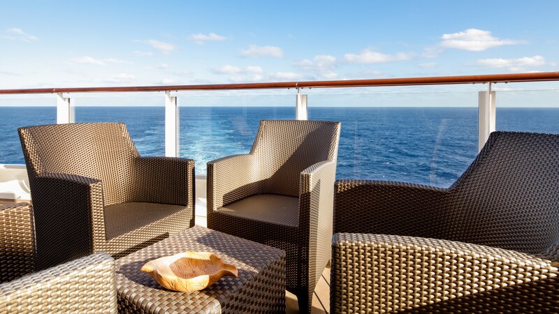 Three wicker chairs and a wicker table sit on a deck with an ocean view