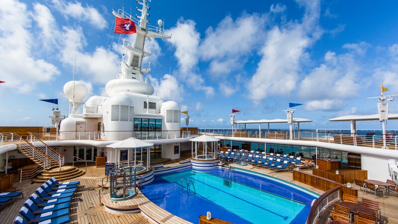 Open pool area containing a rectangular pool flanked by a hot tub on each end and relaxing lounge chairs