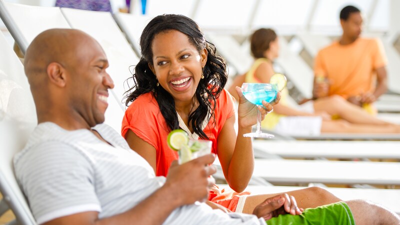 A happy young couple relaxing on lounge chairs enjoying cocktails