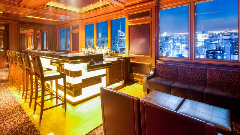 An elegant bar with high back stools near a lounge area with sofas and cocktail tables