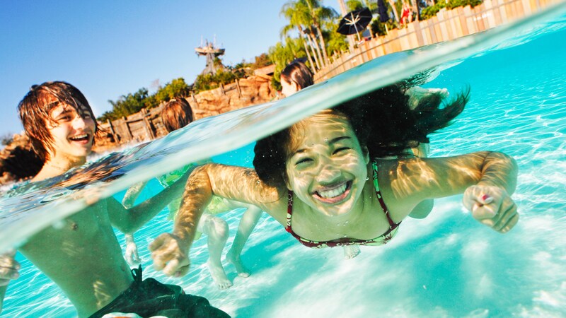 A boy in a pool looks on as a girl swims underwater at Typhoon Lagoon Water Park
