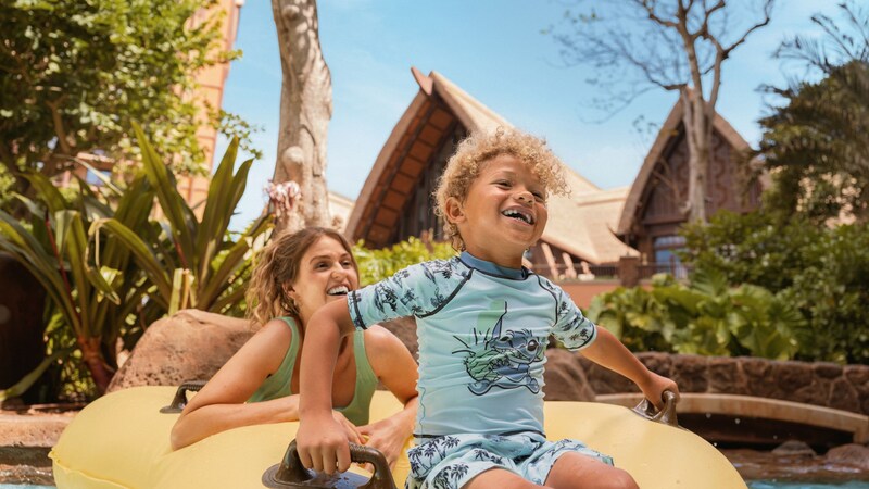 A mother and her young son ride a raft through Waikolohe Stream at Aulani, A Disney Resort and Spa
