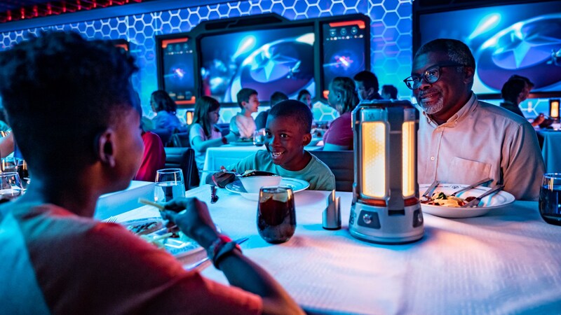 A man and 2 young boys smile at each other while dining inside Worlds of Marvel restaurant