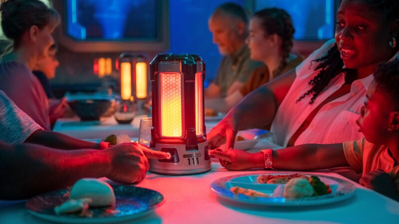 A mother, father and child interacting with a high tech gadget sitting on their table