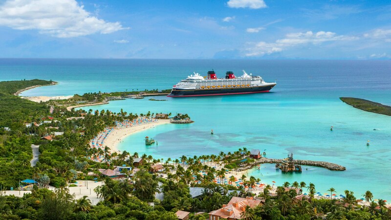 A Disney Cruise Line ship docked at Disney Lookout Cay surrounded by calm waters and sandy beaches lined with palm trees
