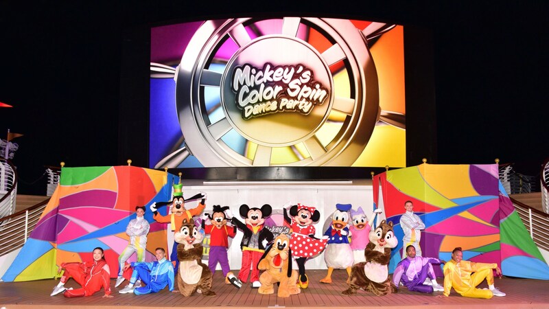 A scene from Mickey’s Color Spin Dance Party featuring Disney Characters and Cast Members posing for a picture on the Funnel Vision Deck Stage of a Disney Cruise Line ship