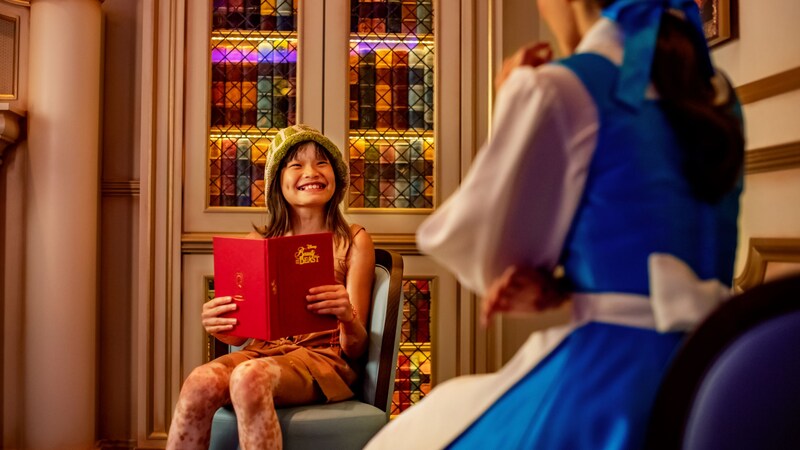 A child holding a book while smiling at the Disney Character Belle from the animated Disney movie Beauty and the Beast 