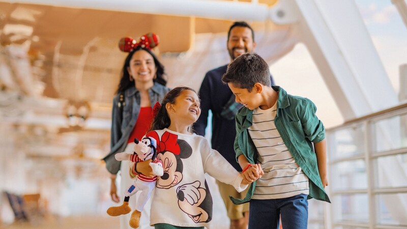 Smiling family in Disney themed attire walking together on the deck of a Disney Cruise Line ship