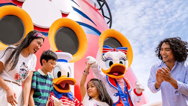 A young family of 4 dancing with Donald Duck and Daisy Duck while on the deck of a Disney Cruise Line ship