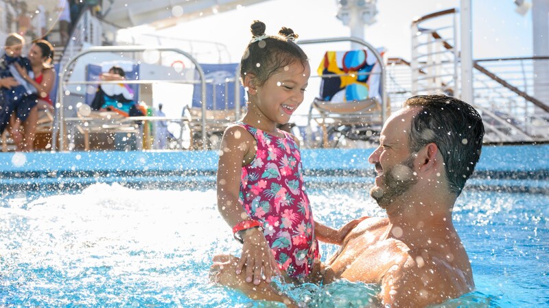 A parent and child playing in a pool on the deck of a Disney cruise ship 