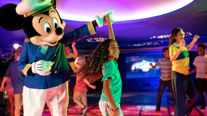Captain Mickey Mouse holding a girl’s hand in the air while she twirls inside Disney’s Oceaneer Club on board the Disney Adventure	