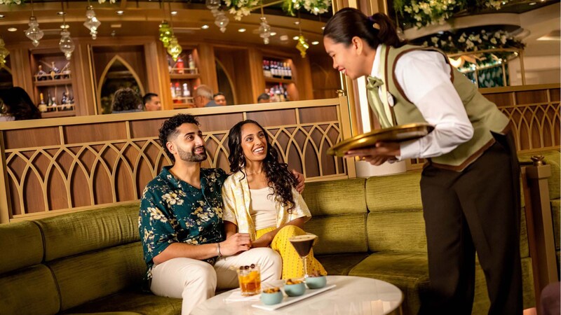 A Cast Member serving Guests beverages at Tiana’s Bayou Lounge on board the Disney Adventure