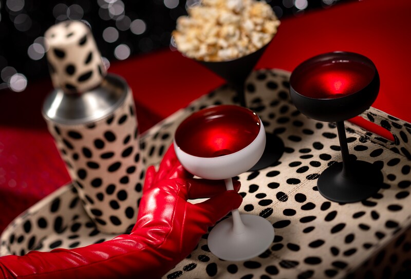 A gloved hand picking up a beverage from a dalmatian spotted tray with a cocktail shaker and a popcorn filled martini glass at De Vil’s lounge