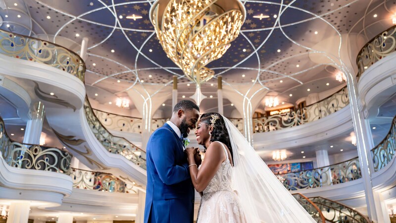A bride and groom smiling and holding hands in the Grand Hall on the Disney Wish