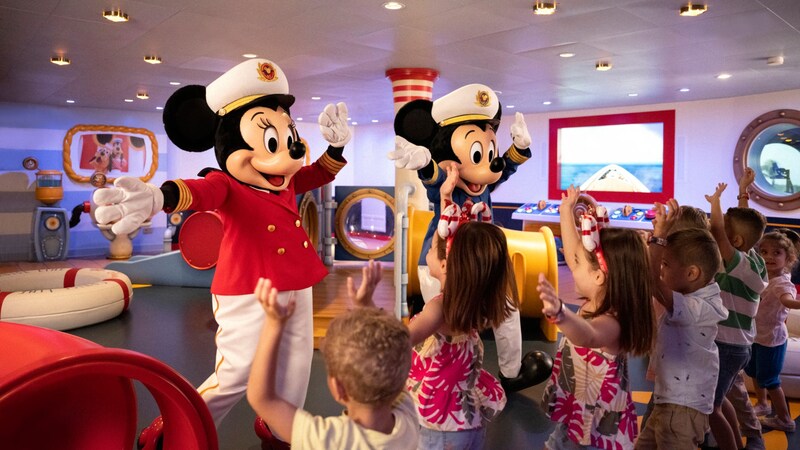 Captain Mickey Mouse and Captain Minnie Mouse dancing with a group of children aboard a Disney cruise ship 