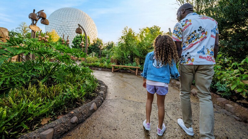 A father and his daughter walking down a garden path near the Spaceship Earth attraction