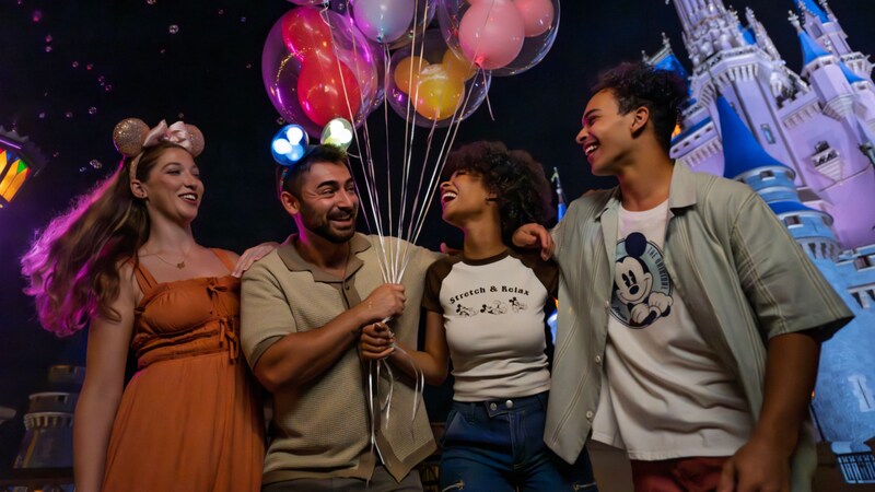 A group of 4 friends gathered together while holding balloons in front of Cinderella Castle at night