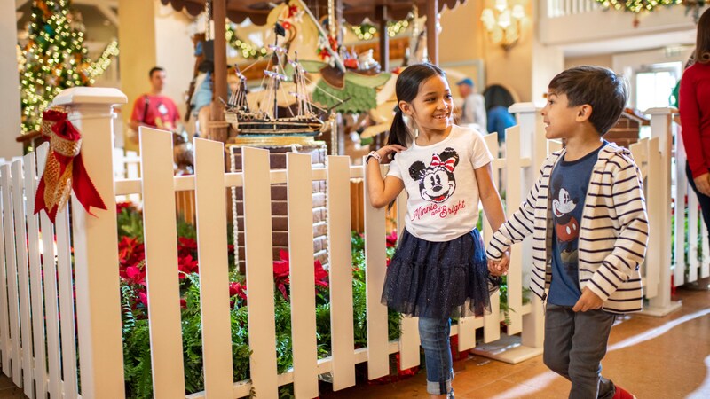 Two young children holding hands while walking near the Gingerbread Carousel at Disney's Beach Club Resort