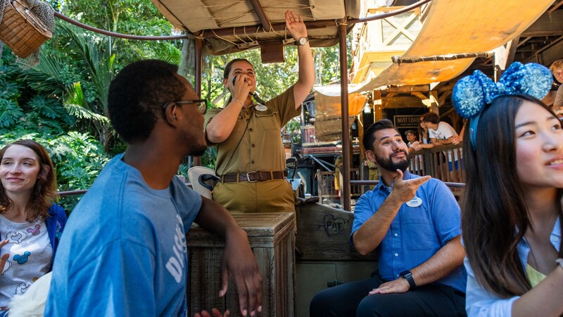 A male Sign Language interpreter narrates the Jungle Cruise on a boat, while a man wearing a hearing aid looks on.