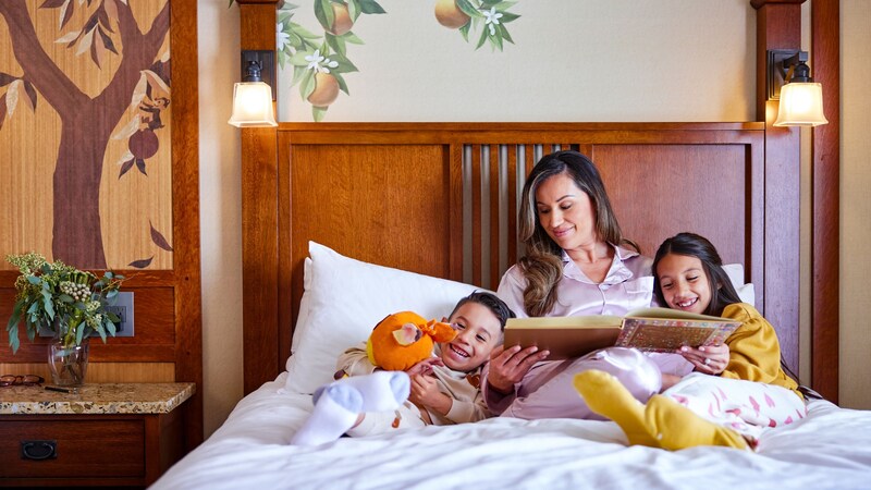 A mother reading to her 2 children in bed at Disney’s Grand Californian Hotel & Spa