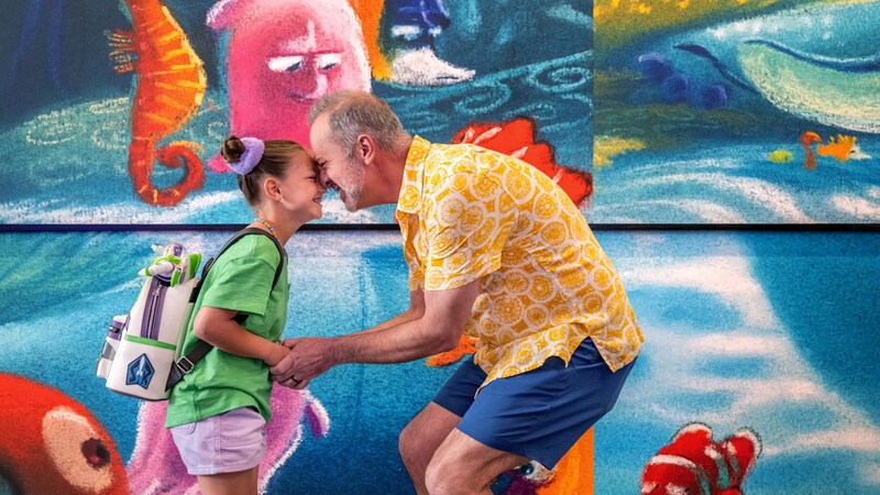 A father and daughter embracing and smiling by the Finding Nemo art wall at Pixar Place Hotel