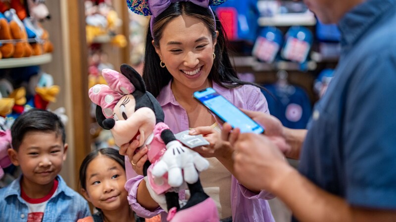 A man looks at a cell phone near 2 children and a woman holding a Minnie Mouse plush