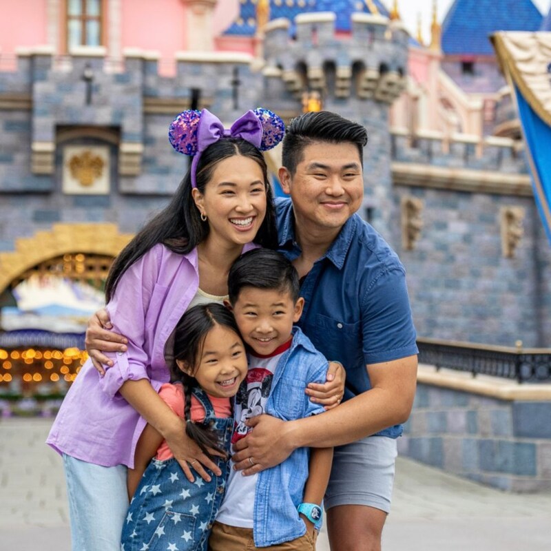 A family poses and grins in front of Cinderella Castle in Disneyland Park