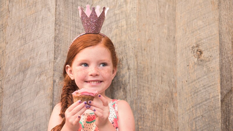 A little girl wears a crown and holds a cupcake